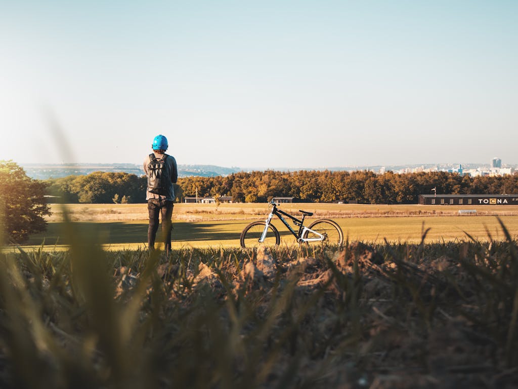 Man with mountain bike stands in a rural field near Prague, enjoying a sunny day.