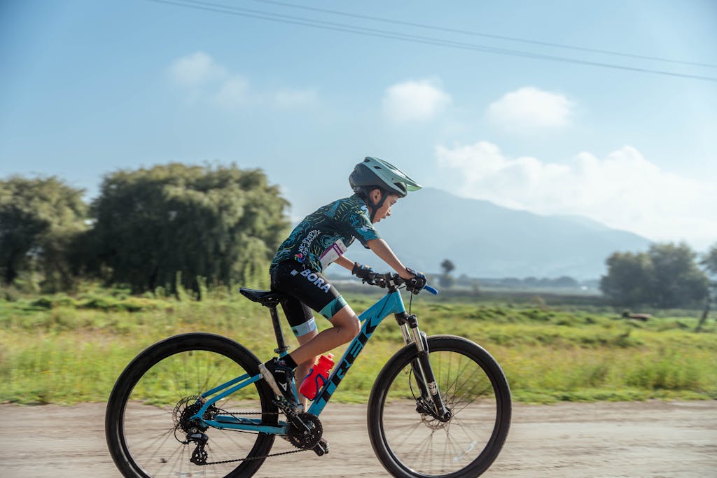 A young boy in sportswear rides a mountain bike on a rural dirt road during a sunny summer day.